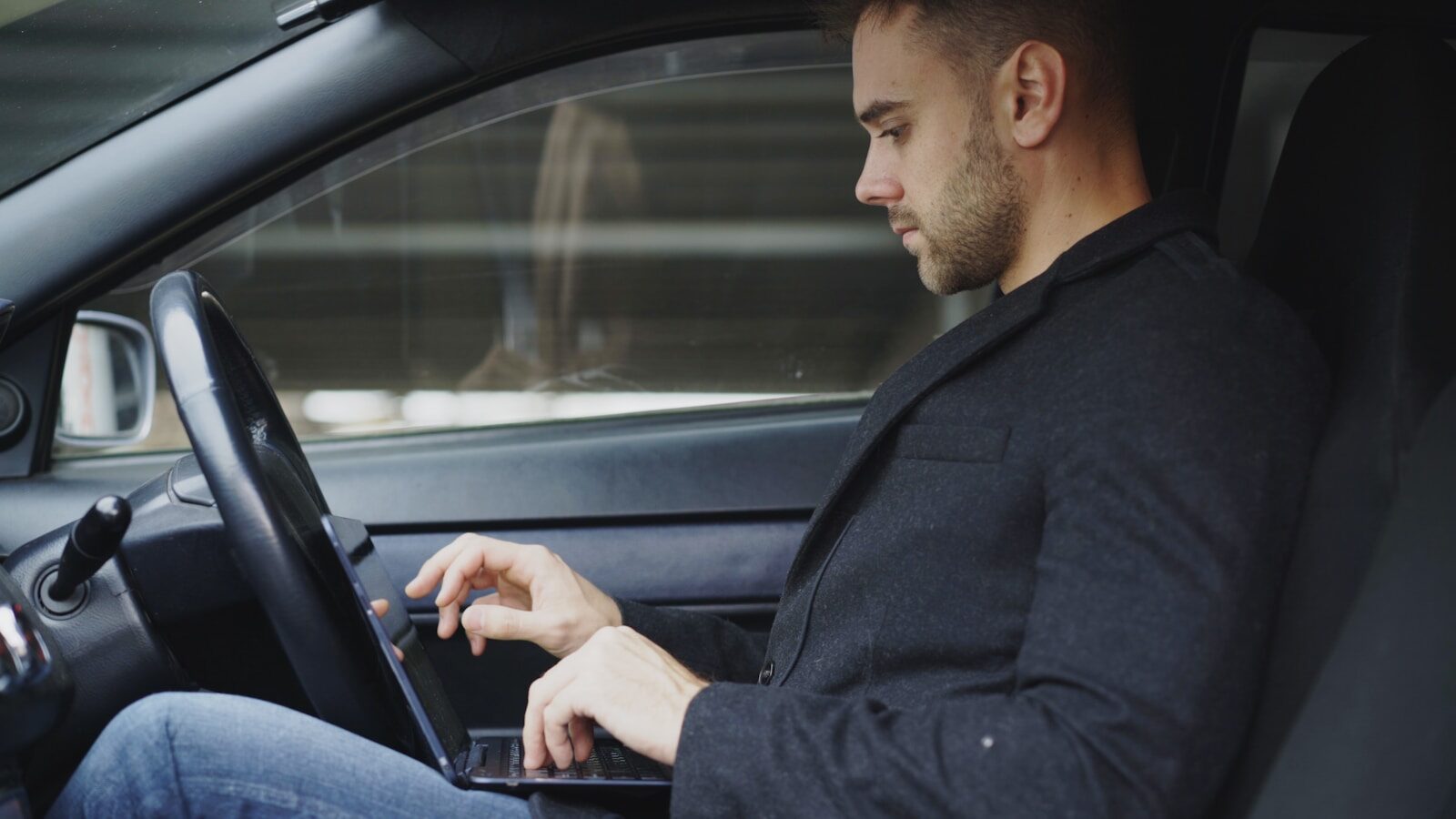 Man working on laptop inside a car.